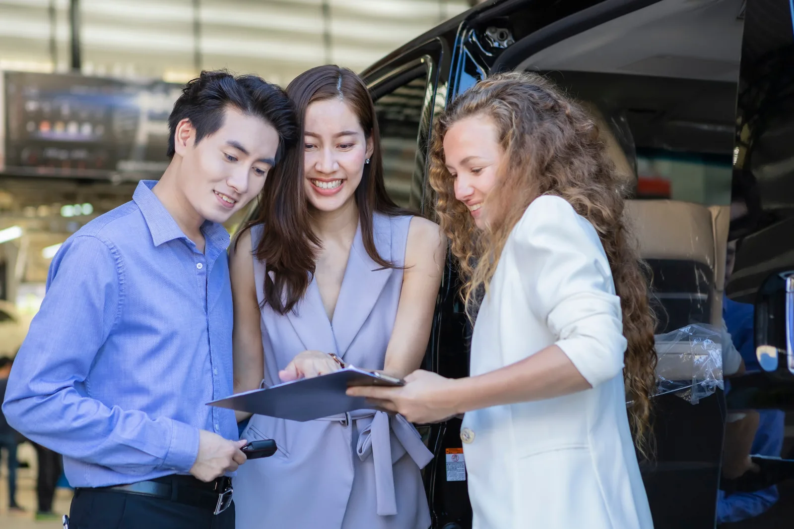 Couple going through paperwork with a dealer beside a black car in a showroom