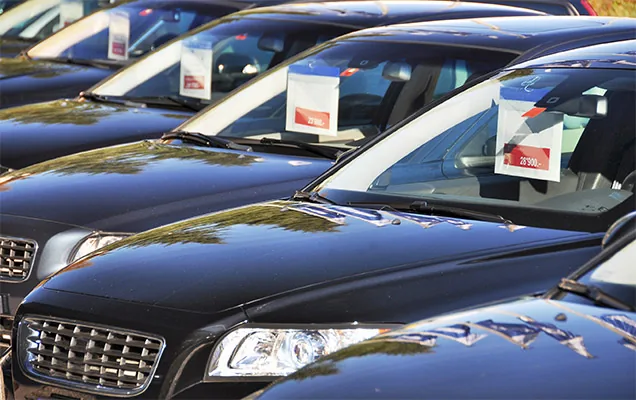 Used cars lined up on a dealer lot with price tags propped in the windscreens
