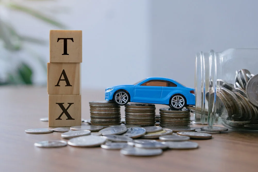 Wooden TAX blocks beside a blue toy car parked on stacks of coins