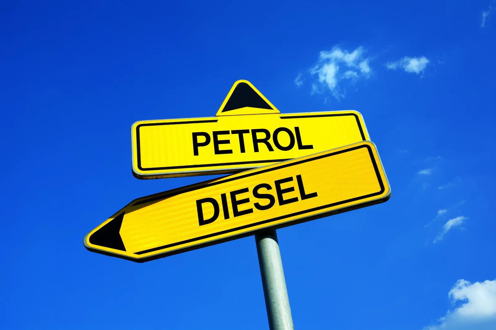 Yellow road signs pointing opposite ways, one marked Petrol and one Diesel