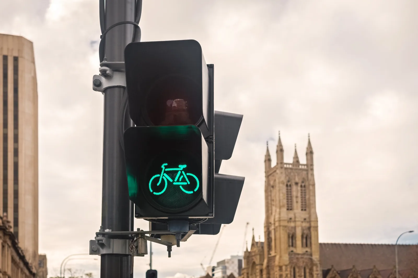 Green bicycle signal at a city intersection with a cathedral tower behind