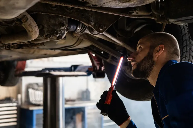 A mechanic using a light to inspect the underside of a raised car during a safety inspection.
