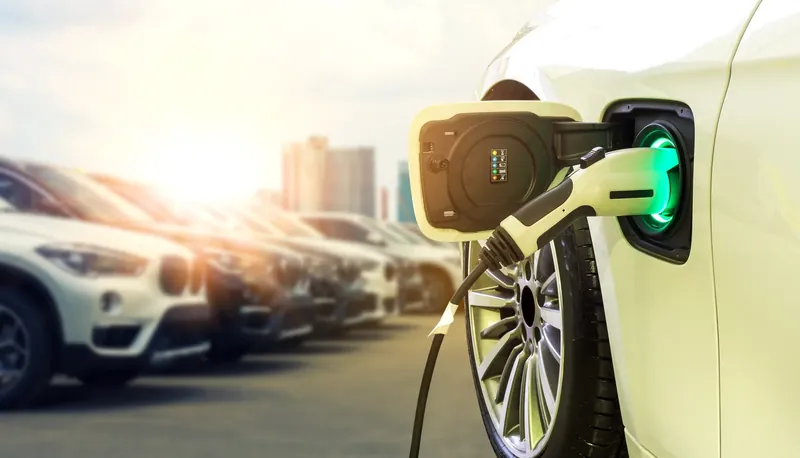Electric car plugged in and charging beside a row of cars at sunset