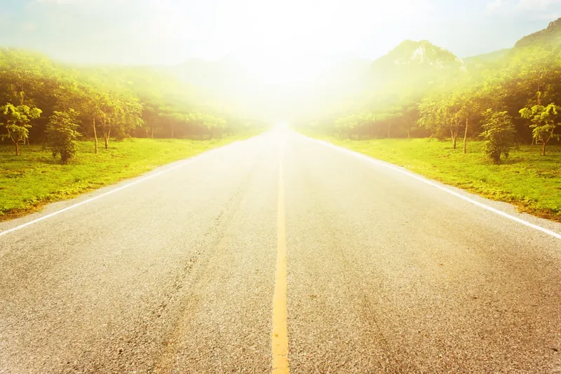 Empty country road running towards green hills in bright summer sun