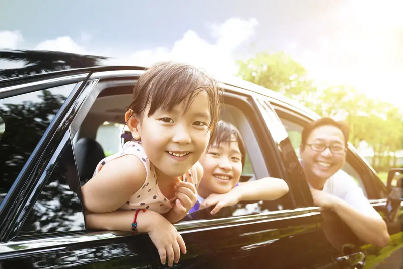 Two children and their dad leaning out of the windows of a black family car