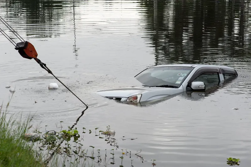 Silver car half submerged in floodwater being winched back to the bank