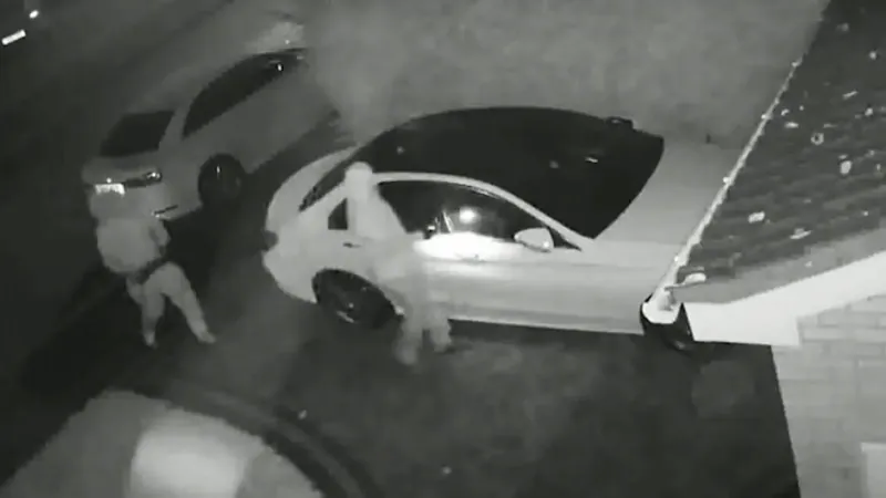 Night CCTV still of two people beside a car parked in a driveway