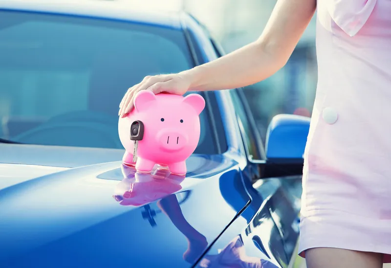 Pink piggy bank with a car key resting on the bonnet of a blue car
