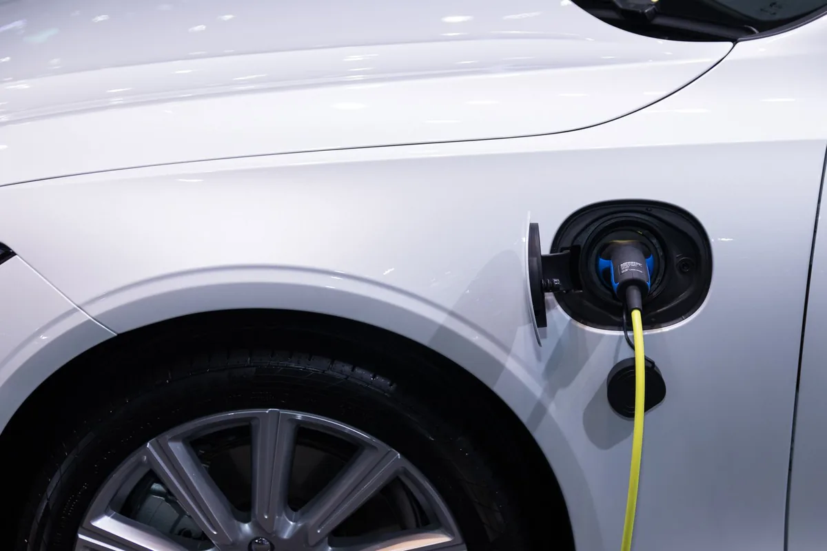 Electric car plugged into a public DC fast-charging station with the charging cable connected to the charge port