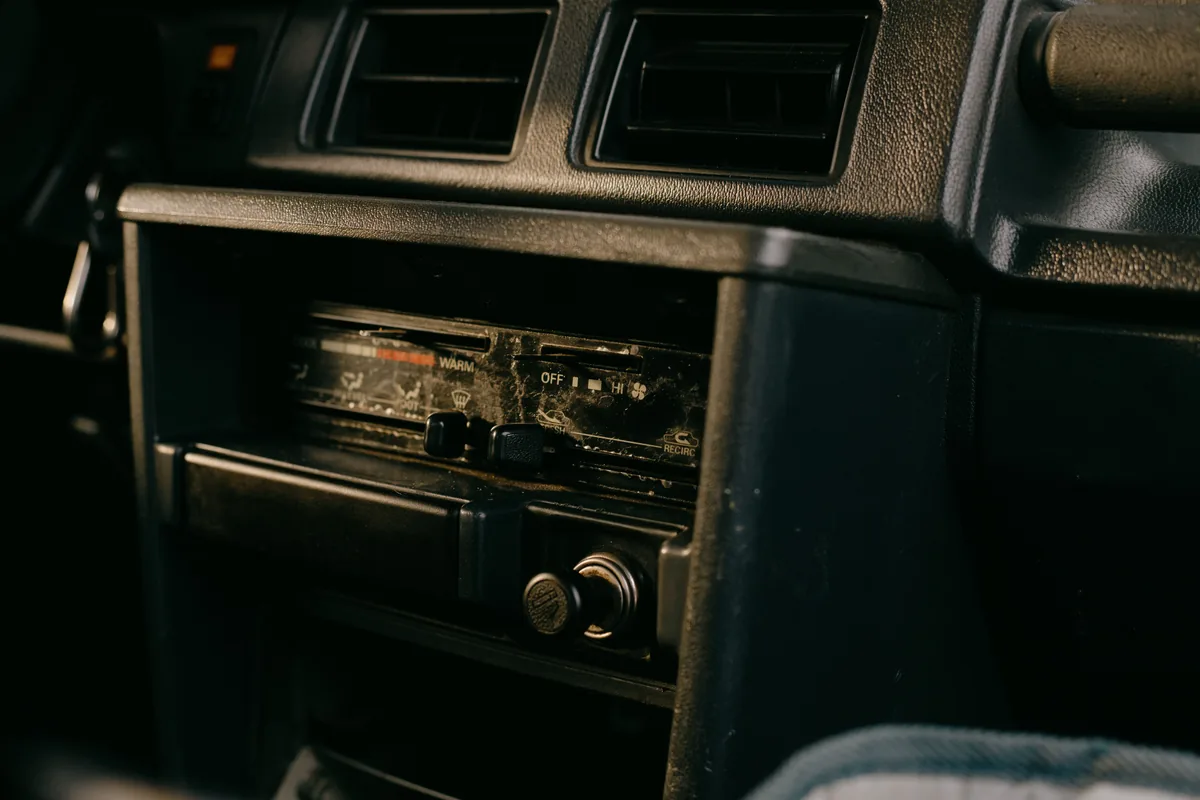 An older car's dashboard with a small factory radio and physical buttons, no touchscreen